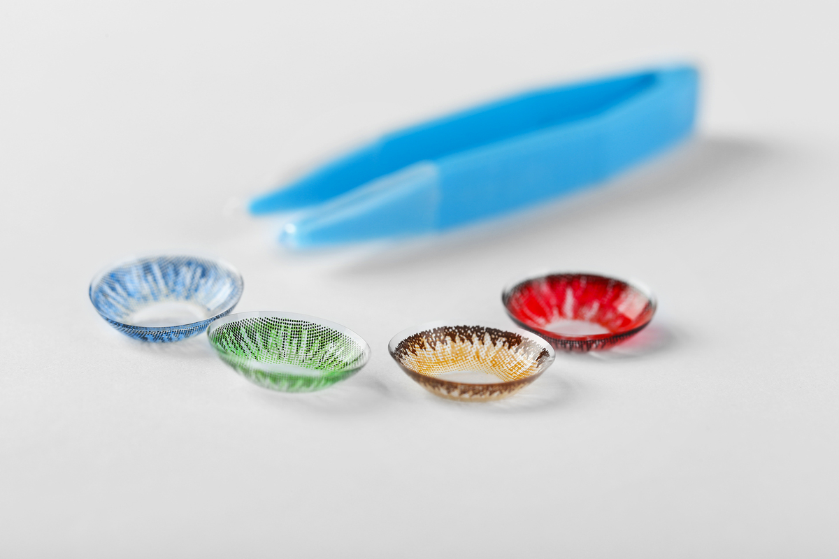 Blue, green, brown and red contact lenses with tweezers on white background